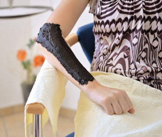 Moorpackung in einer spaähnlichen Umgebung – eine dunkle, dickflüssige Masse wird auf die Haut aufgetragen, um die Muskeln zu entspannen und die Haut zu pflegen